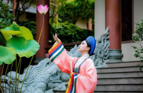 Free A woman in a vibrant kimono reaches gracefully for a lotus flower, embodying elegance and tradition. Stock Photo