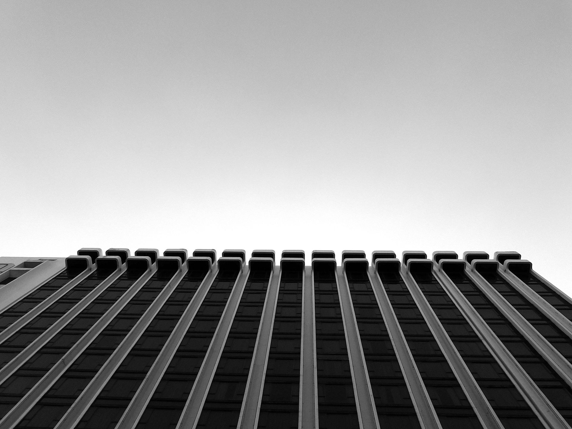 Black and white photo of a tall, modern building in Hong Kong viewed from below with symmetrical lines.