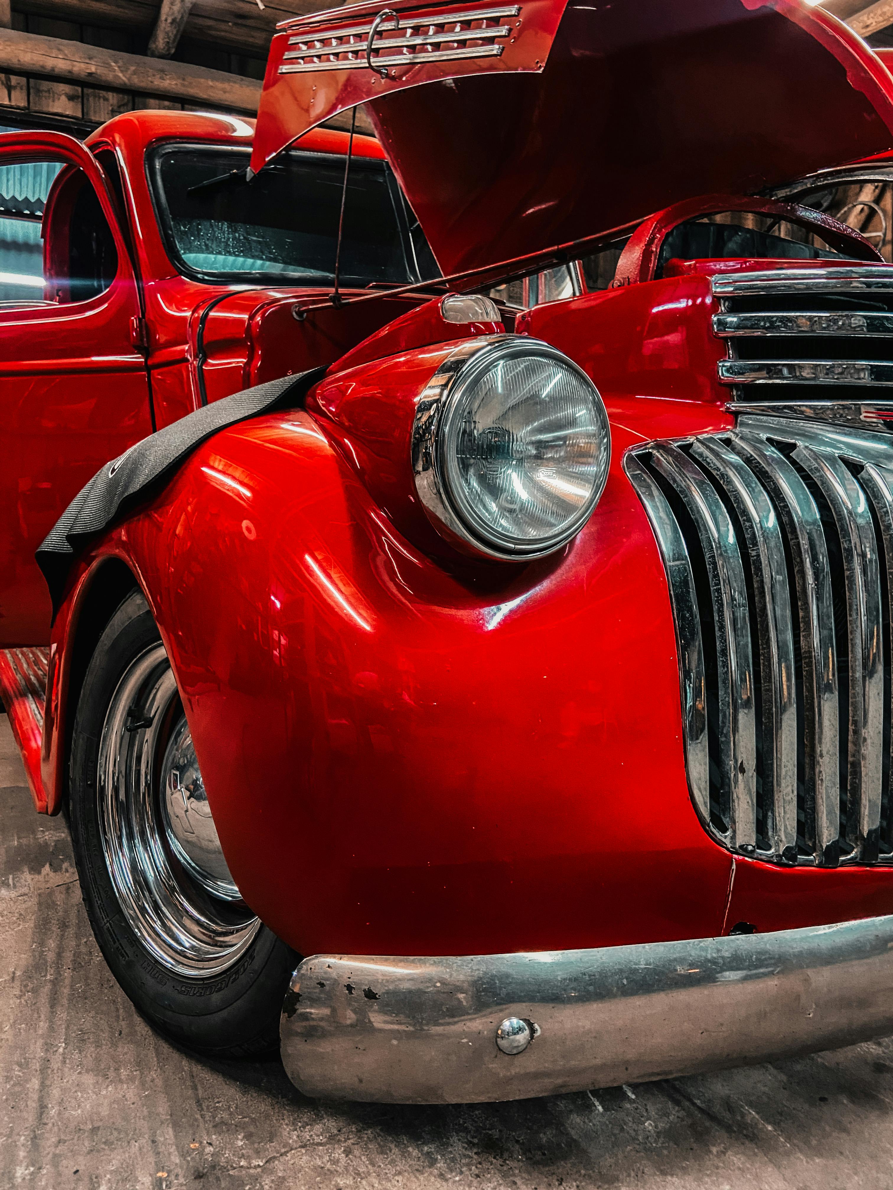 Close-up of a shiny red vintage car with open hood, showcasing classic design in a garage.