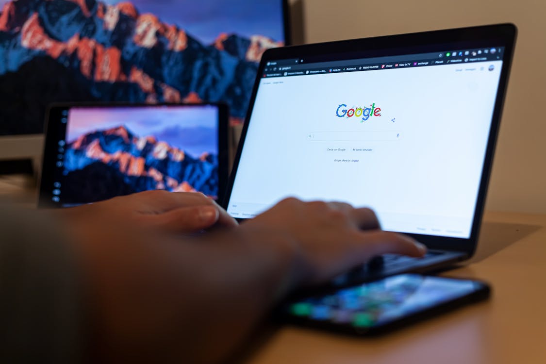 Een persoon die Google Chrome gebruikt op een laptop met een mobiel apparaat en andere gadgets op een tafel