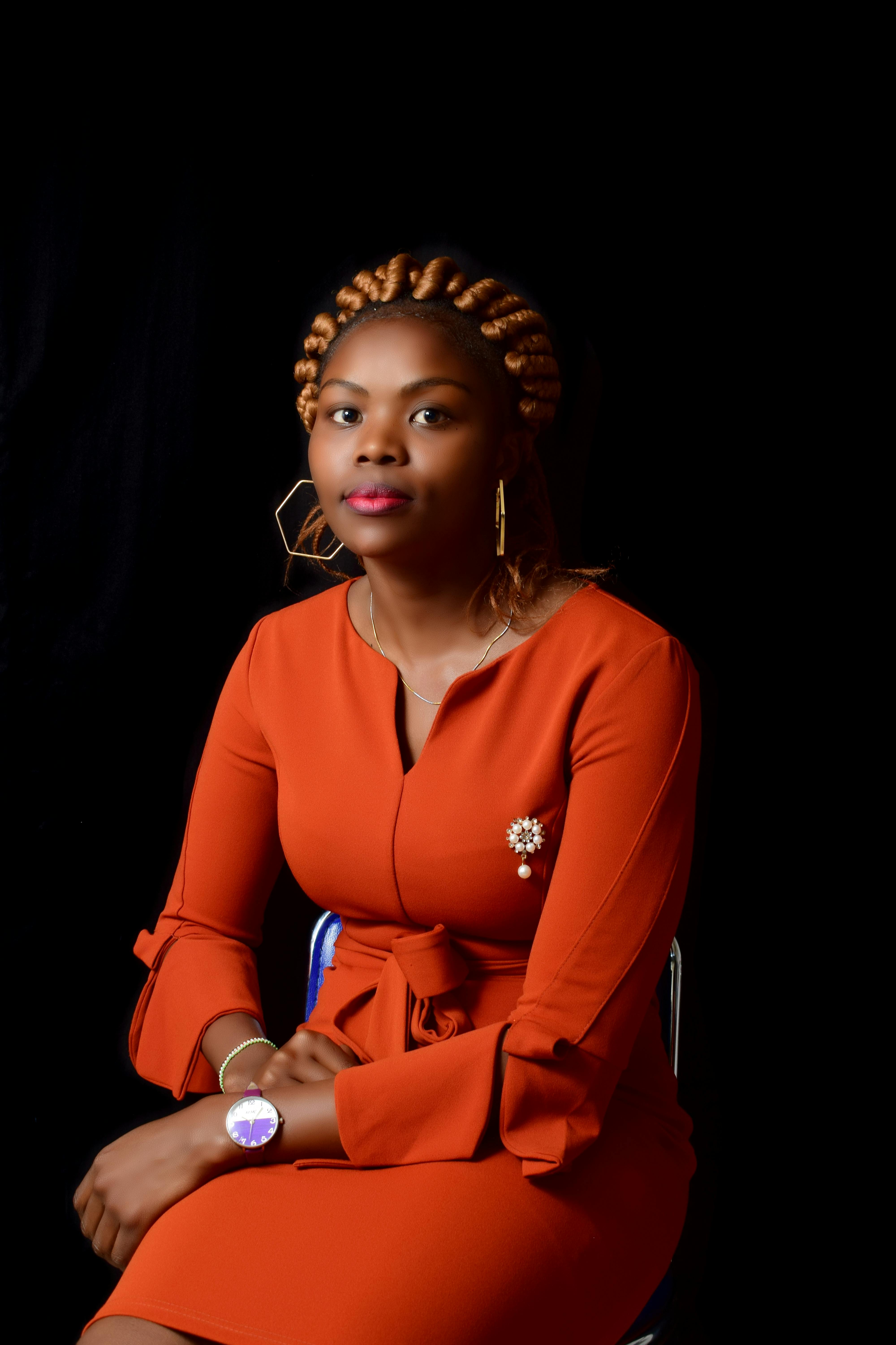 Elegant African woman sitting gracefully in a brown dress against a black background.