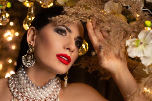 Charming female in luxury pearl necklace standing in room with festive decorations