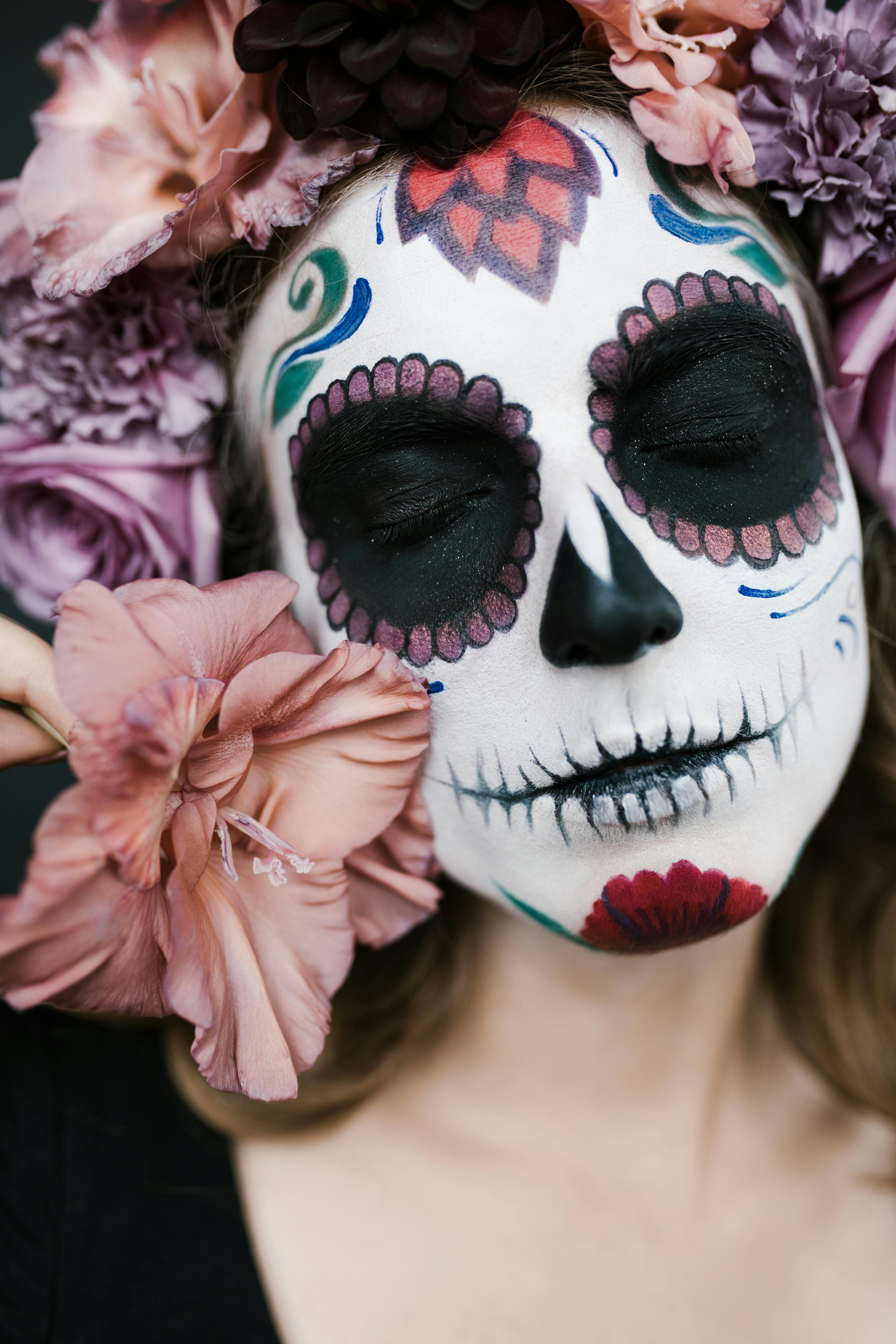 Close-up of a woman's face with sugar skull makeup and flower headdress celebrating Day of the Dead.