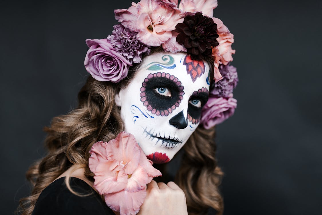 Free Young female with sugar skull make up and hair decorated with flowers for celebrating Halloween Stock Photo