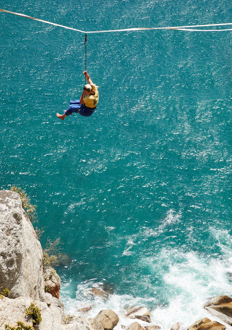 Unrecognizable Woman Riding Zipline Over Sea