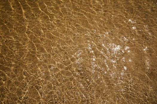 Rippling shallow water with sunlight reflections on a sandy seabed, creating a calm and serene texture.