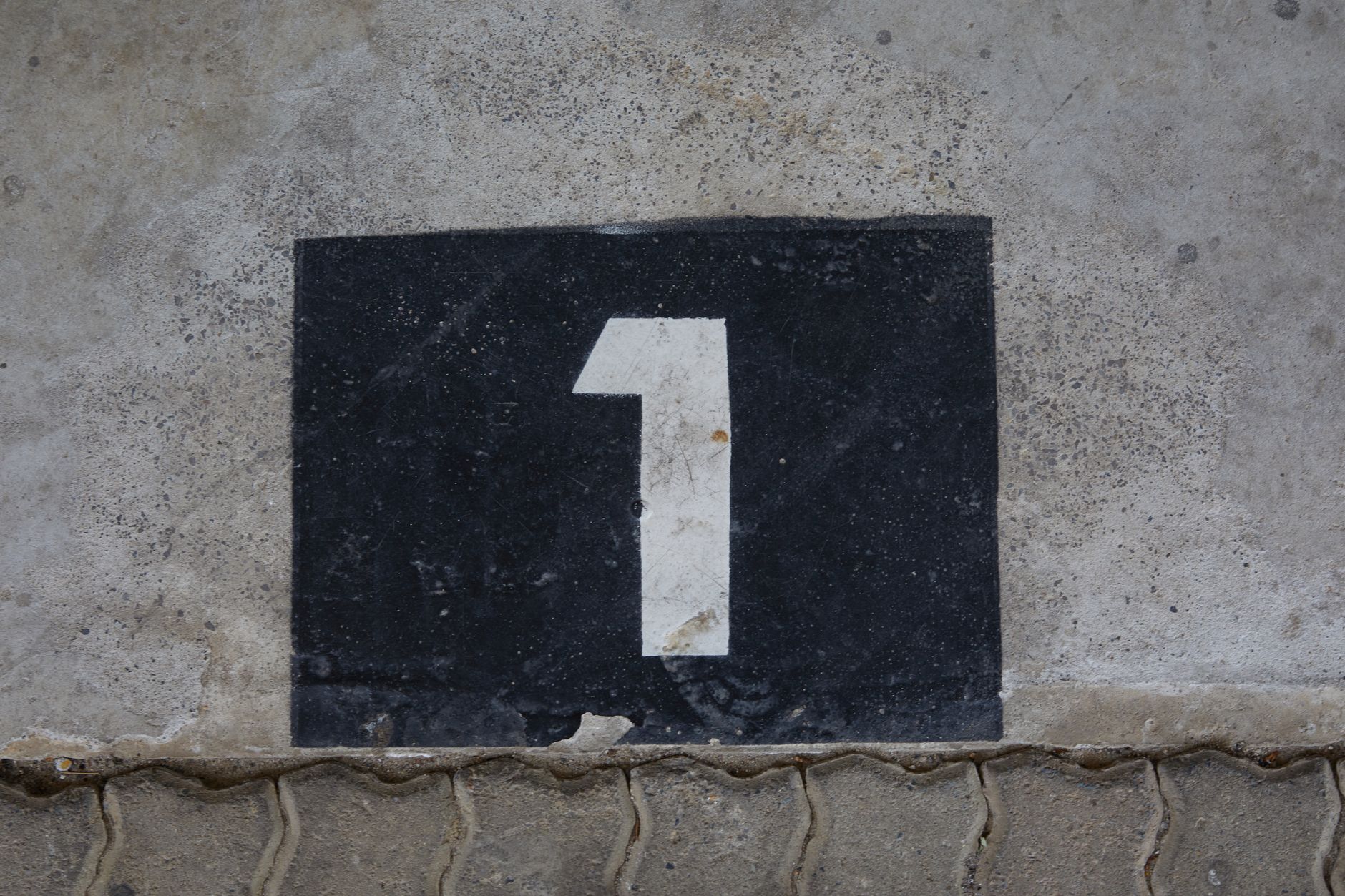 A weathered concrete wall with a bold number one painted on a black rectangular background.