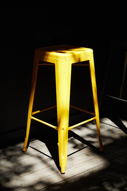 Free Yellow bar chair placed on wooden floor in dark room with minimal light Stock Photo