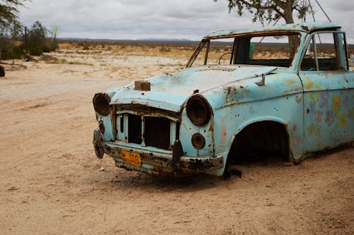 Free Old rusty broken abandoned car without wheels and radiator placed in sandy terrain near tree Stock Photo