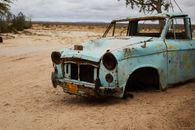Old rusty broken abandoned car without wheels and radiator placed in sandy terrain near tree