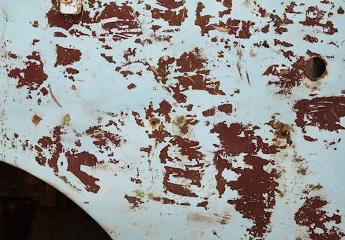 From above of shabby abandoned metal construction with round hole and rusty spots among white paint