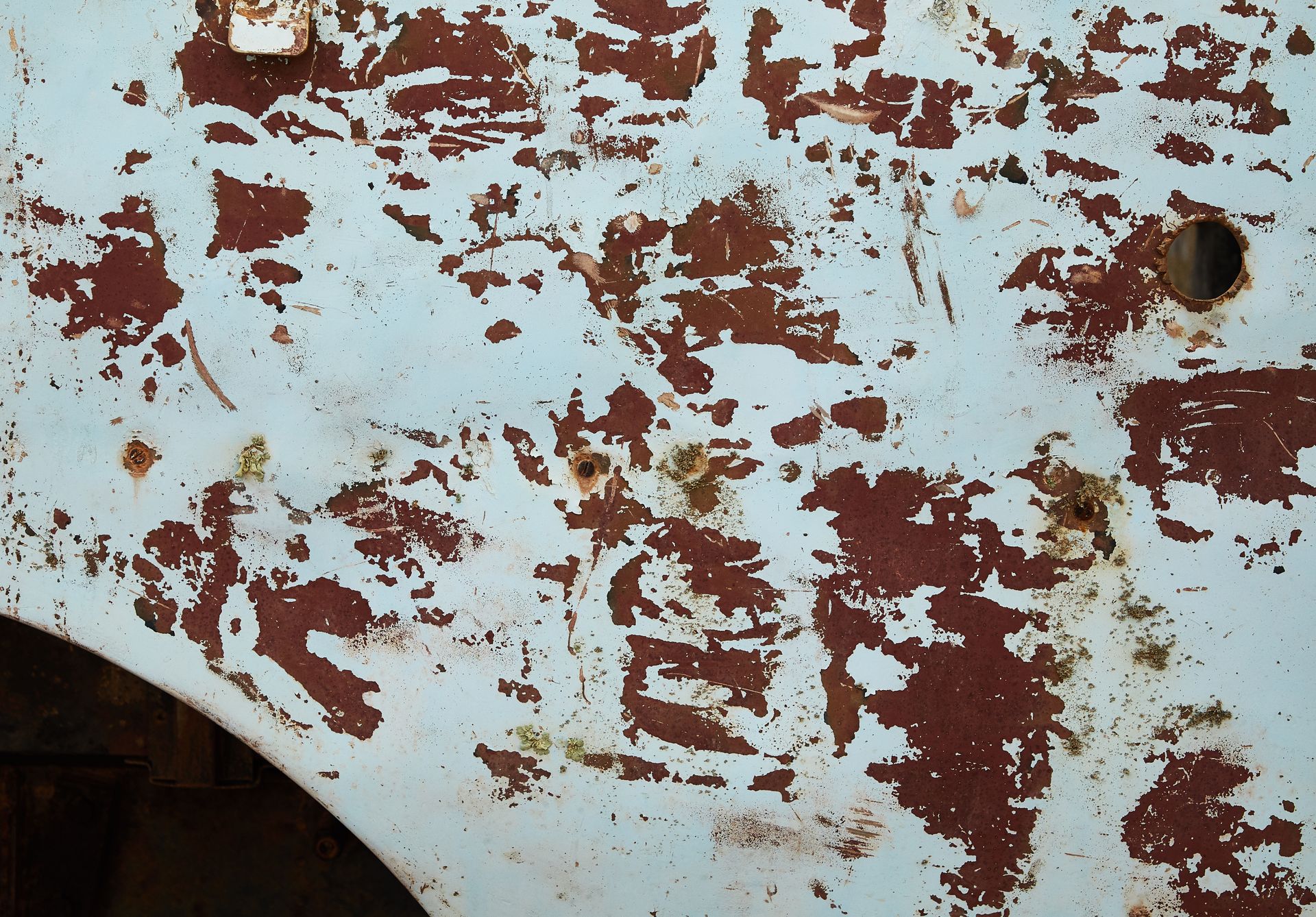 From above of shabby abandoned metal construction with round hole and rusty spots among white paint