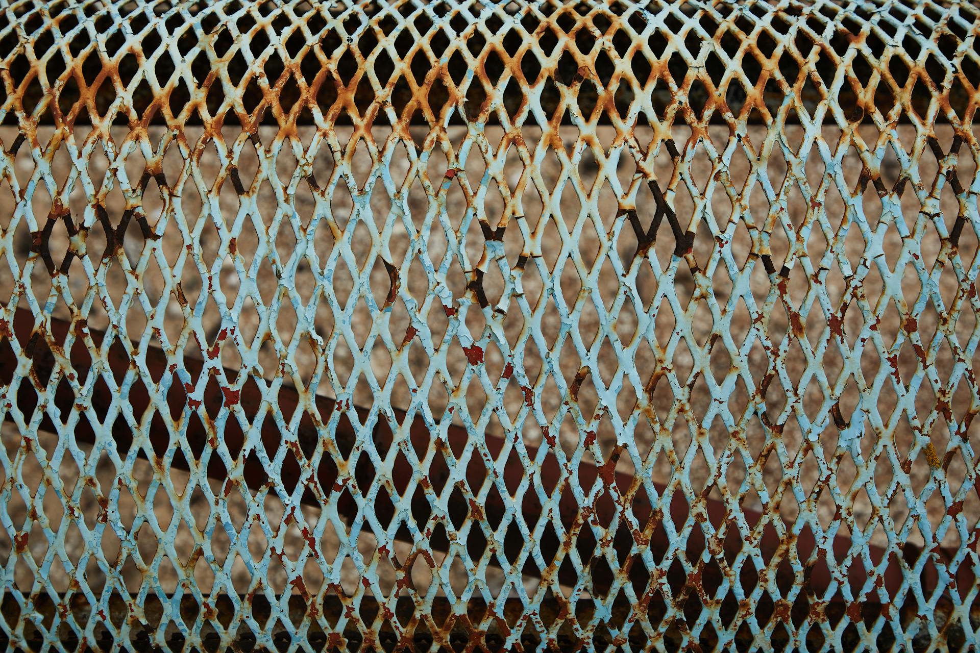 Full frame of weathered blue metal lattice with rusty parts and spots placed on fence in daytime