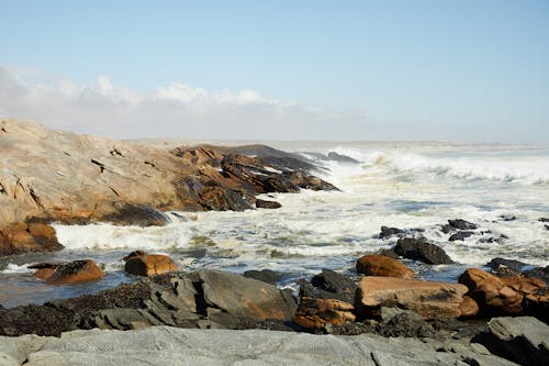 Endless ocean washing uneven coast with rocks under cloudy blue sky in daytime