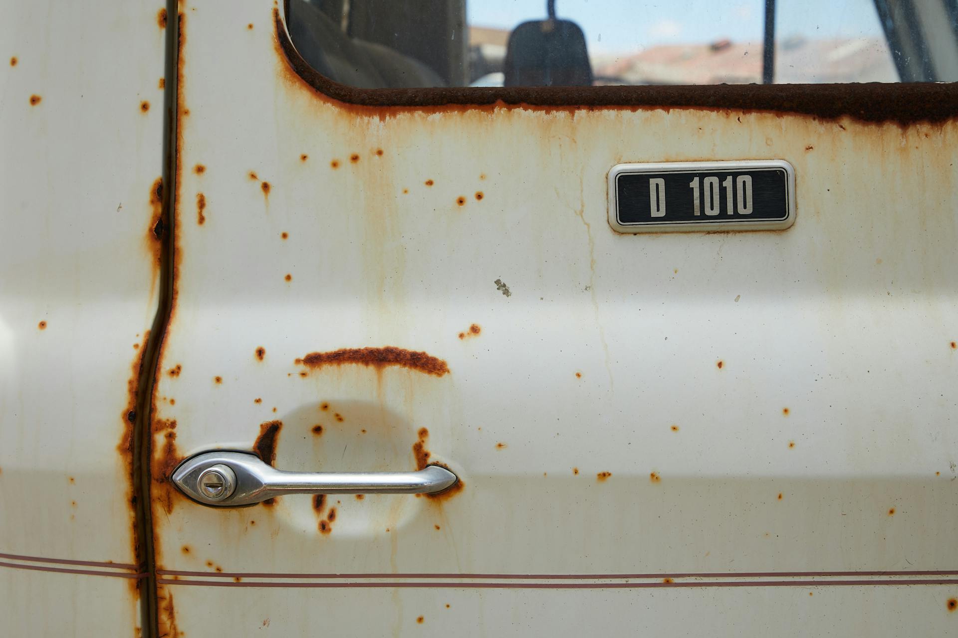 Detailed view of an old rusty car door with metal handle and worn textures, depicting age and nostalgia.