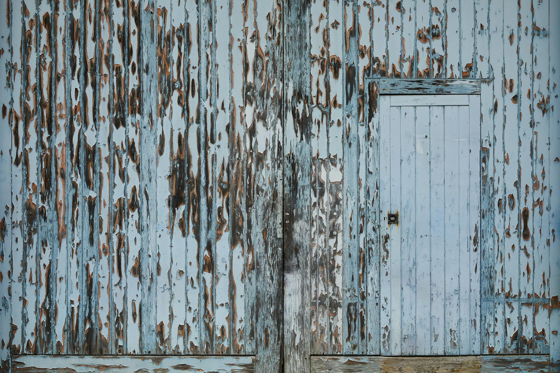 Entrance of aged damaged abandoned wooden warehouse with peeling white paint on wall