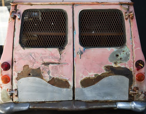 Old automobile with broken taillights and windows with lattice covered with rust and scratches