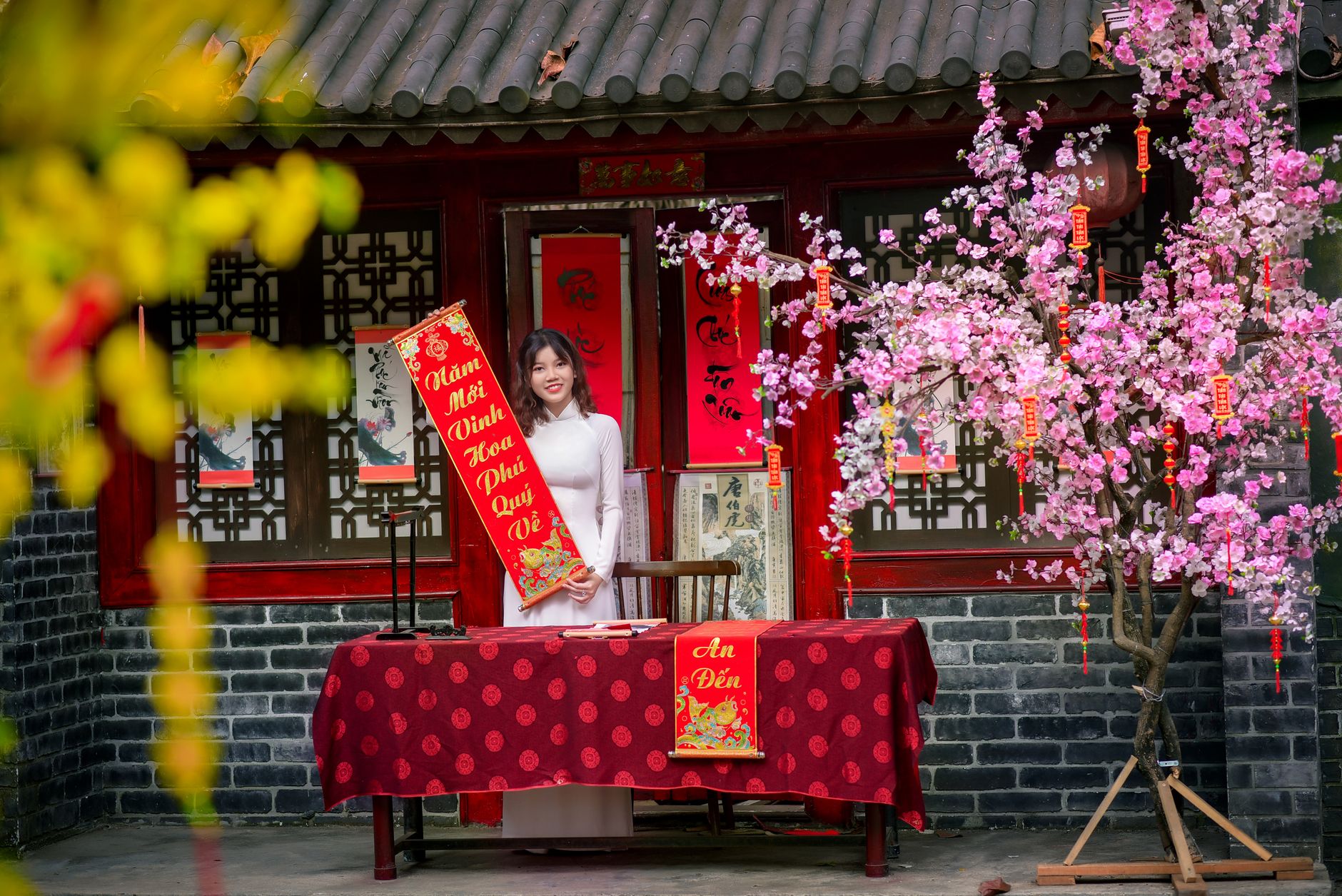 Asian woman in ao dai celebrates Vietnamese New Year with traditional decorations and cherry blossoms.