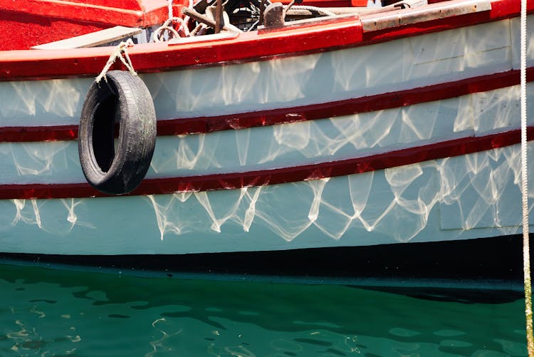 Boat With Reflection Of Water And Tire Hanging On Rope