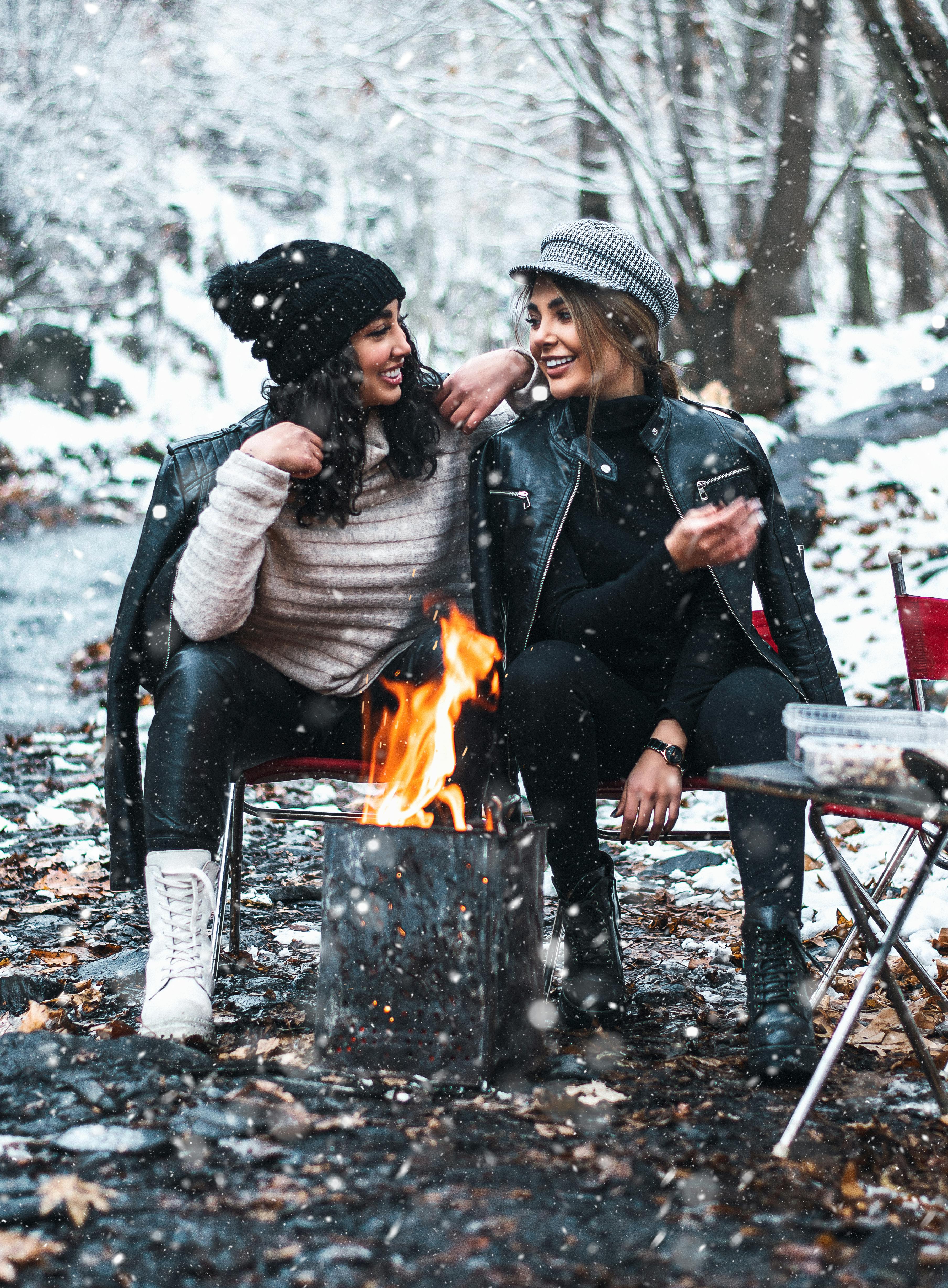 young girlfriends in leather jackets sitting near campfire and communicating