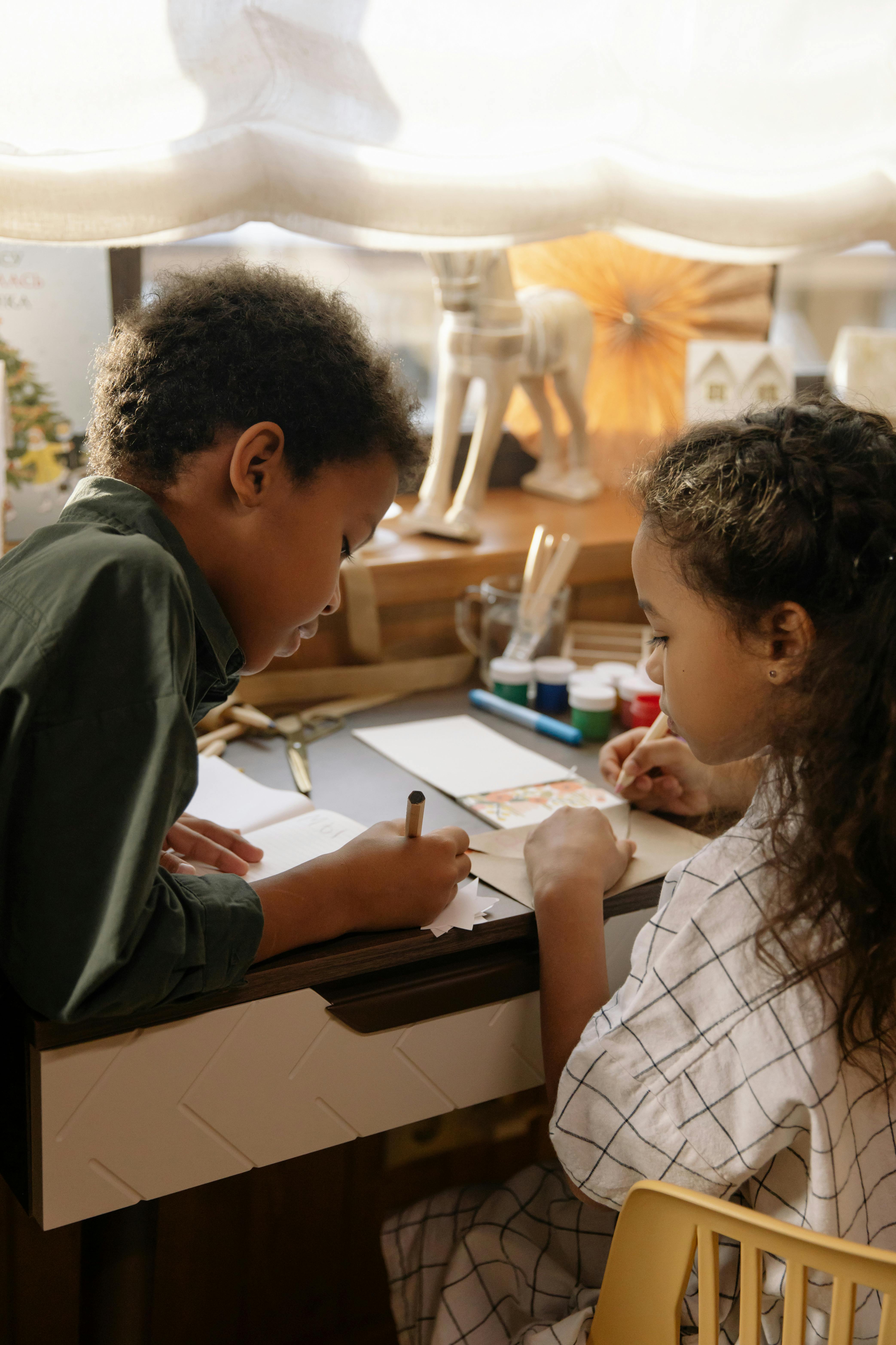 a girl watching her brother write on a paper