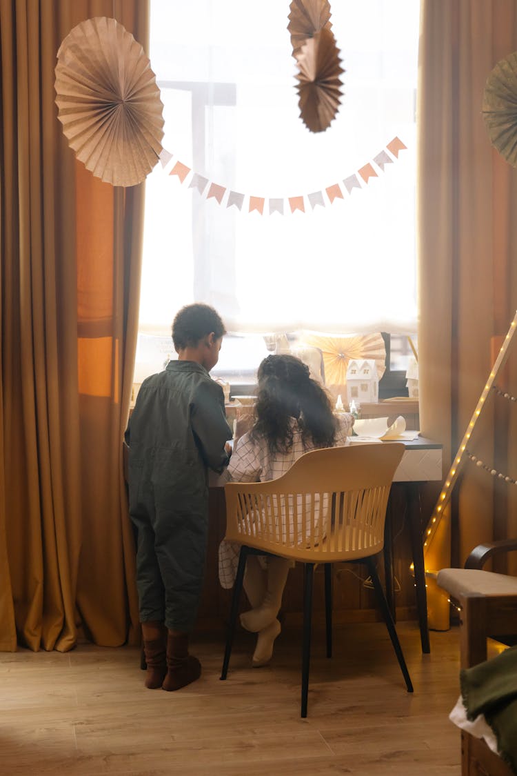 Two Kids Standing And Sitting By The Table