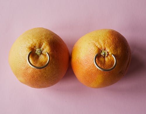 Fresh mandarins with earrings placed on pink surface