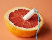 From above of half of sliced ripe grapefruit with tampon in center showing use of feminine product during menstruation