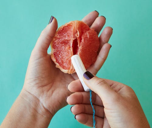 From above of crop anonymous female demonstrating on sliced ripe grapefruit correct use of tampon against blue background