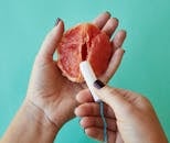 From above of crop anonymous female demonstrating on sliced ripe grapefruit correct use of tampon against blue background