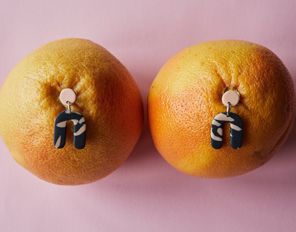 Top view of trendy earrings stucking in fresh ripe tangerines placed on pink surface in studio