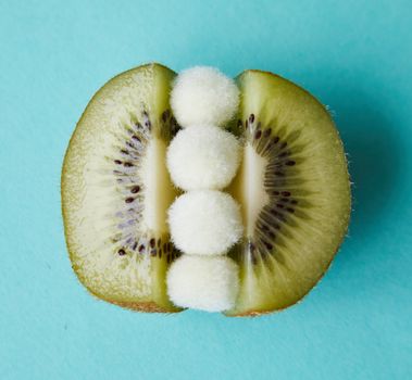 Fur pom poms between halves of kiwi on blue surface