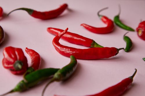Free Ripe various red and green spicy chili peppers placed on pink surface in light place Stock Photo