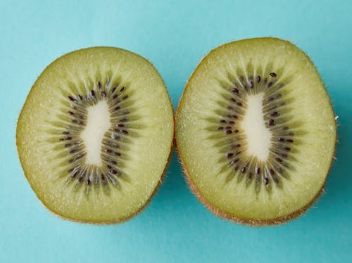 Free From above of green halves of kiwi with black seeds placed on blue background Stock Photo