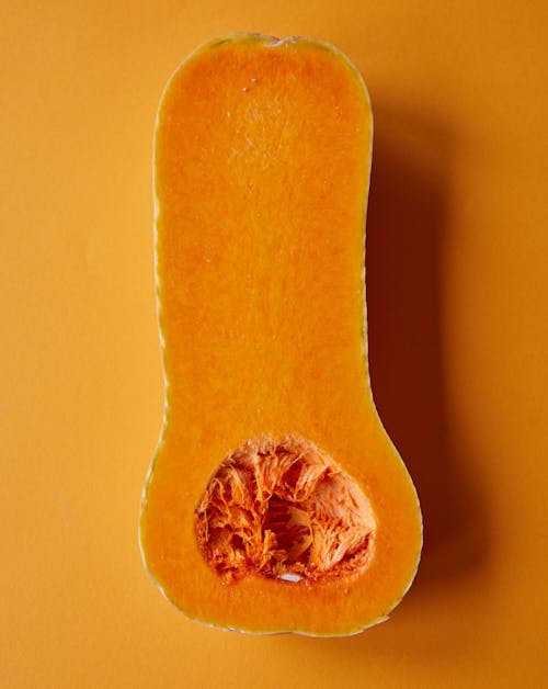 Top view composition of bright fresh ripe half of butternut squash placed on orange surface