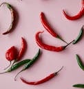 Top view composition of various fresh multicolor chili peppers with green stems placed on pink board