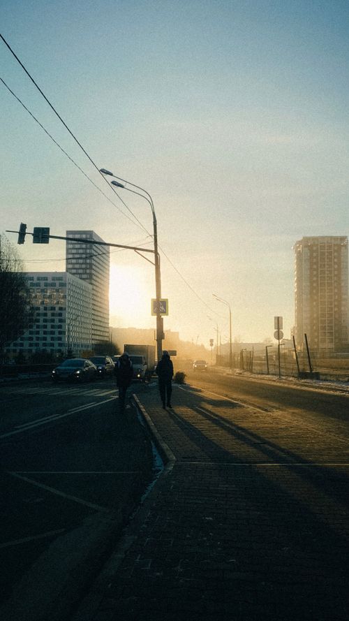 Free Silhouettes of people walking together along asphalt road with traffic light in downtown of contemporary megapolis at sunrise Stock Photo