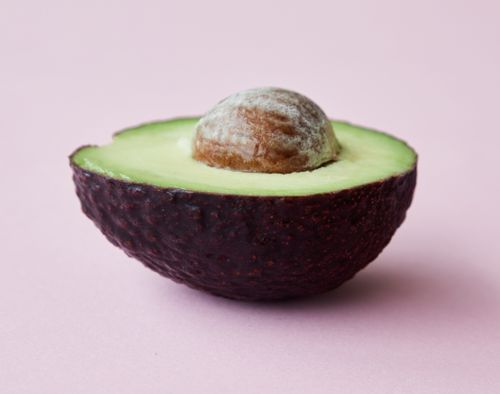 Free Half of cut ripe avocado with green pulp and large seed placed on light pink background Stock Photo