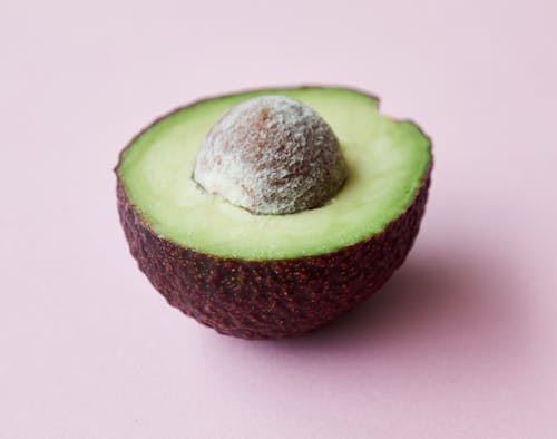High angle of half of fresh ripe avocado with seed on purple background