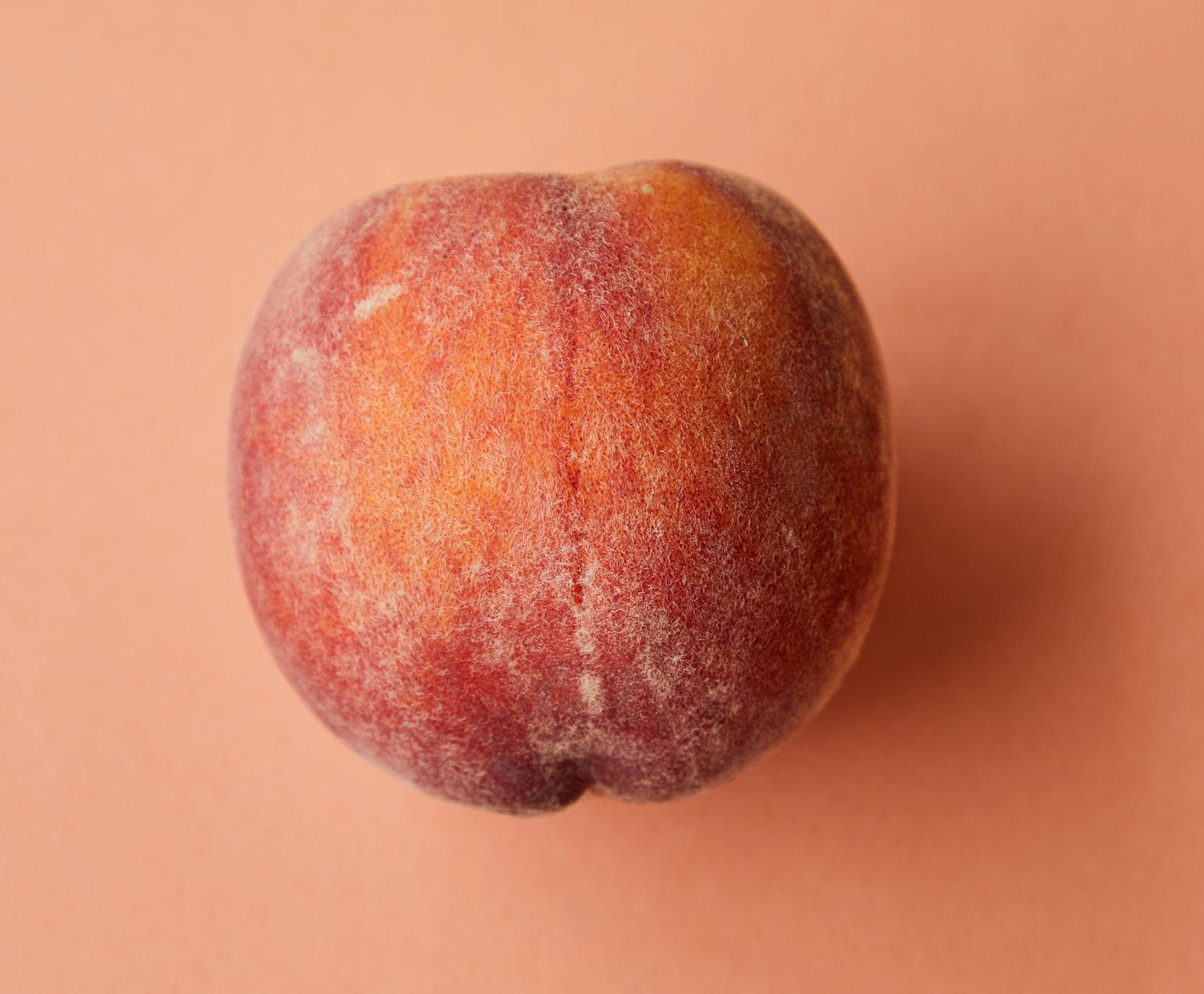 Fresh juicy pink peach on pink surface