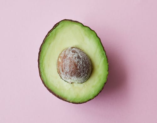 Free From above of half of fresh raw ripe avocado with seed on purple background Stock Photo