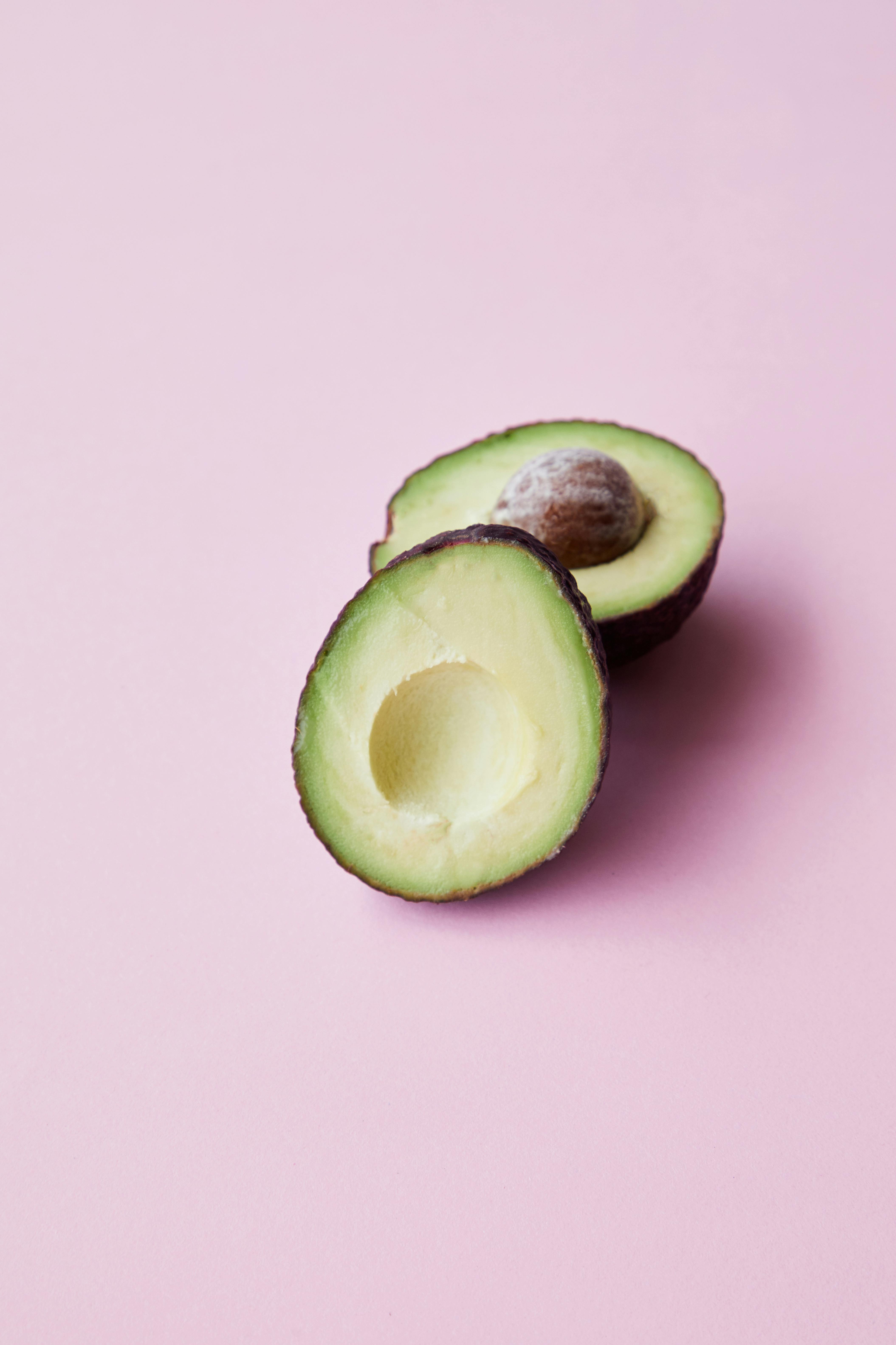 halved ripe avocado placed on pink background