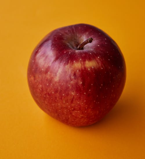 High angle of ripe shiny whole red apple placed on bright orange background