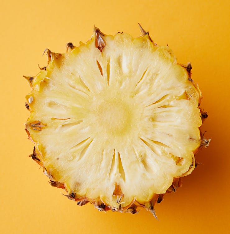 Free Top view half of appetizing ripe juicy exotic pineapple placed on yellow background Stock Photo