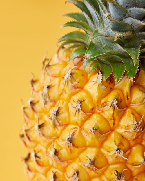 Free Tasty ripe pineapple with rough verdant leaves on bright yellow background of studio Stock Photo
