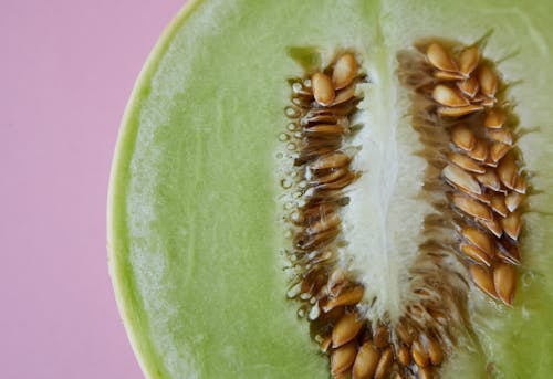 Top view of half cut fresh juicy melon with seeds placed on pink background