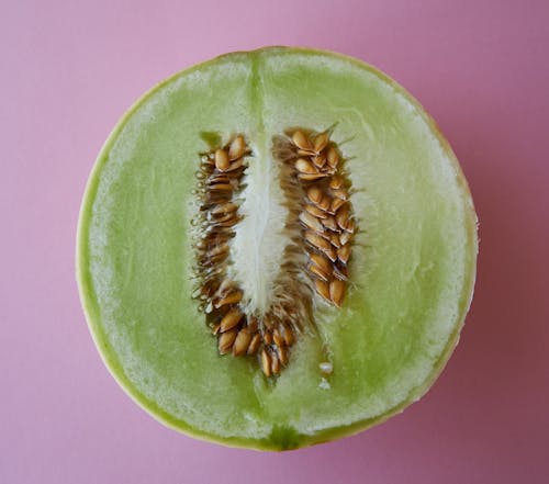 Top view of fresh half cut melon with seeds placed on pink background