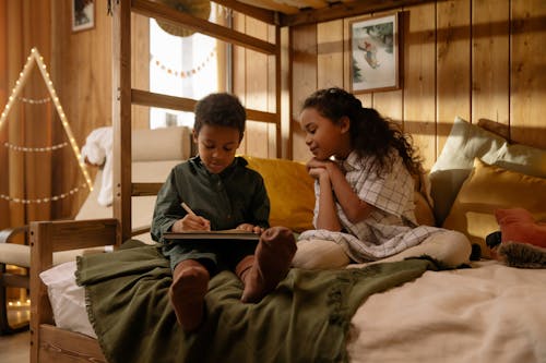 A Girl Watching Her Brother Write on a Book