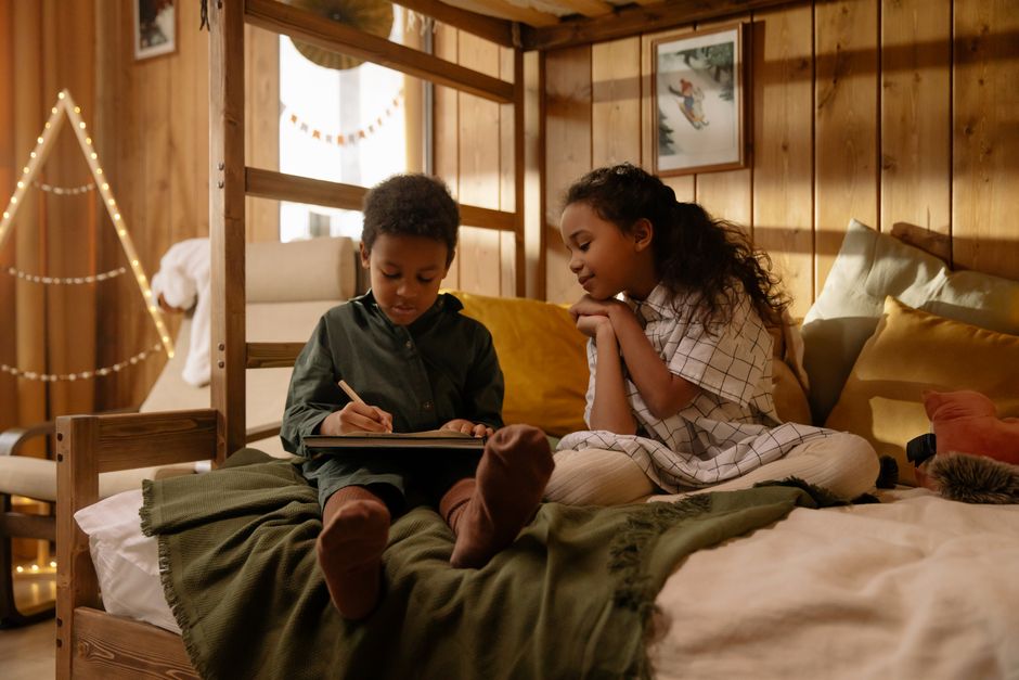 Zwei Kinder sitzen auf einem Bett und lesen ein Buch in einem gemütlich eingerichteten Schlafzimmer.