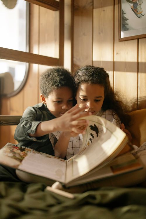 Free Two children reading a book together on a cozy couch by the window. Stock Photo